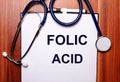 On a wooden background lies a stethoscope and a sheet of paper with the inscription FOLIC ACID. Flat lay. Medical concept