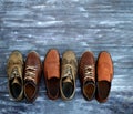 On a wooden background are three pairs of brown shoes. One pair of leather sneakers is very worn, the second is in good Royalty Free Stock Photo