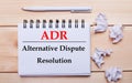 On a wooden background, a white notebook with the inscription ADR Alternative Dispute Resolution, a white pen and crumpled white Royalty Free Stock Photo