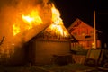 Wooden barn burning at night. High orange fire flames, dense smoke from under tiled roof on dark sky, trees silhouettes and reside Royalty Free Stock Photo