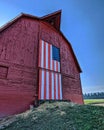 A wooden barn with a door with the American flag design, with grass in front of it on a sunny day Royalty Free Stock Photo