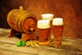 Wooden barrel, three different glasses of light beer, hops and ears of wheat on a wooden table against a brown wall Royalty Free Stock Photo