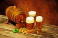 Wooden barrel, three glasses of light beer with foam, ears of barley and hops on a wooden table Royalty Free Stock Photo