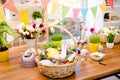 Wooden basket with easter composition, sweets, choco, gingerbread standing on table decorated with easter colored eggs and flowers