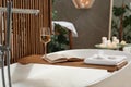 Wooden bath tray with glass of wine, open book, massage stones and towel on tub indoors. Relaxing atmosphere Royalty Free Stock Photo