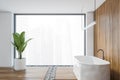 Wooden bathroom with white bathtub and a plant near large window in modern flat Royalty Free Stock Photo