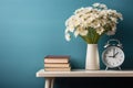 wooden bedside table with a vase with bouquet of white flowers, books and an alarm clock, against a blue wall Royalty Free Stock Photo