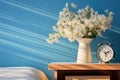 wooden bedside table with a vase of white flowers and an alarm clock, against a blue wall with morning light Royalty Free Stock Photo