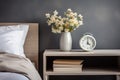 wooden bedside table with a vase of white flowers, books and an alarm clock, against a gray wall Royalty Free Stock Photo