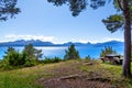 A wooden bench with benches on the bank of a picturesque wide blue river on the forest edge overlooking the mountains on the Royalty Free Stock Photo