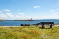 Wooden bench on the coastal shoreline in Inishbofin with the lighthouse on Gun Rock and a sailboat in the background