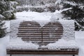 Wooden bench covered with snow and heart drawn on it. Heart drawn on snow on bench in park. Royalty Free Stock Photo