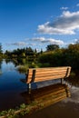 Wooden bench on the flooded shore of Larson Lake, reflections of blue sky and clouds