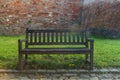 A wooden bench by the footpath stands on the grass. Behind the bench is a high brick wall