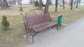 A wooden bench on a forged metal base and an urn are installed on a tiled area near a walkway in a park next to a grassy lawn and Royalty Free Stock Photo