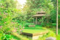 Wooden bench on fresh green carpet grass yard, smooth lawn beside a brown gazebo under flower blooming trees in beautiful garden Royalty Free Stock Photo