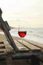 Wooden bench with glass of wine on sandy sea beach