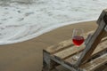 Wooden bench with glass of wine on sandy sea beach