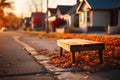 A wooden bench on a leaf-strewn sidewalk at sunset, houses lining the quiet street. Royalty Free Stock Photo