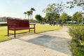 Wooden bench with long line of shadow on walking pathway in small peaceful park with green lawn and palm trees on beautiful summer Royalty Free Stock Photo