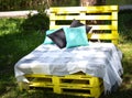 Wooden bench made of yellow pallets of freight cargo cases for sittin with pillows and plaid in the park. The concept of