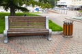 A wooden bench with a nearby trash can.