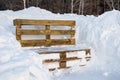 Wooden bench from pallets in a snowdrift after a snowfall in a park in the forest. Snowfall and drifts symbol