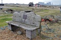 A wooden bench on the pebbles of Dungeness beach surrounded by discarded items from the fishermen