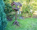Garden bird table in front of lush green trees and hedges in a country garden Royalty Free Stock Photo
