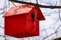 A wooden birdhouse, built with your own hands and painted with colored paint, hangs attached to a tree without leaves.