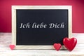 Wooden blackboard with red hearts and written sentence in german Ich liebe dich, which means I love you, in red background Royalty Free Stock Photo