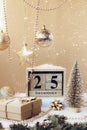 Wooden block calendar with 25 december date, Christmas decorations and falling snow on beige background