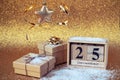 Wooden block calendar with 25 december date, Christmas decorations and gift boxes on golden background with sparkles