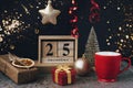 Wooden block calendar with 25 december date, Christmas decorations, red cup, gift boxes on black background