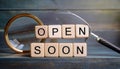 Wooden block with message, open soon with magnifying glass