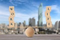 Wooden block with words work and life on wooden seesaw balancing on wood desk with city background