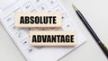 Wooden blocks with the ABSOLUTELY ADVANTAGE Iie on a light background on a white calculator. Nearby is a black handle. Business