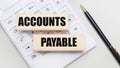 Wooden blocks with the ACCOUNTS PAYABLE Iie on a light background on a white calculator. Nearby is a black handle. Business