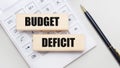 Wooden blocks with the BUDGET DEFICIT Iie on a light background on a white calculator. Nearby is a black handle. Business concept