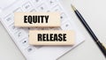 Wooden blocks with the EQUITY RELEASE Iie on a light background on a white calculator. Nearby is a black handle. Business concept