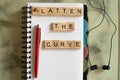 Wooden blocks with flatten the curve on them with a white sprial bound office note book Royalty Free Stock Photo