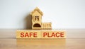 Wooden blocks form the words `safe place` near miniature house. Wooden table. Beautiful white background, copy space