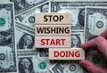 Wooden blocks form the words `stop wishing start doing` on beautiful background from dollar bills. Male hand. Business and start