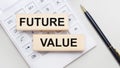 Wooden blocks with the FUTURE VALUE Iie on a light background on a white calculator. Nearby is a black handle. Business concept