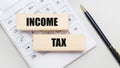 Wooden blocks with the INCOME TAX Iie on a light background on a white calculator. Nearby is a black handle. Business concept