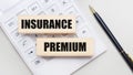 Wooden blocks with the INSURANCE PREMIUM Iie on a light background on a white calculator. Nearby is a black handle. Business