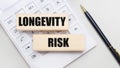 Wooden blocks with the LONGEVITY RISK Iie on a light background on a white calculator. Nearby is a black handle. Business concept