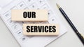 Wooden blocks with the OUR SERVICES Iie on a light background on a white calculator. Nearby is a black handle. Business concept