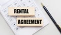 Wooden blocks with the RENTAL AGREEMENT Iie on a light background on a white calculator. Nearby is a black handle. Business