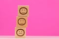 Wooden blocks with smile faces symbols on pink background, evaluation, Increase rating, Customer experience satisfaction.